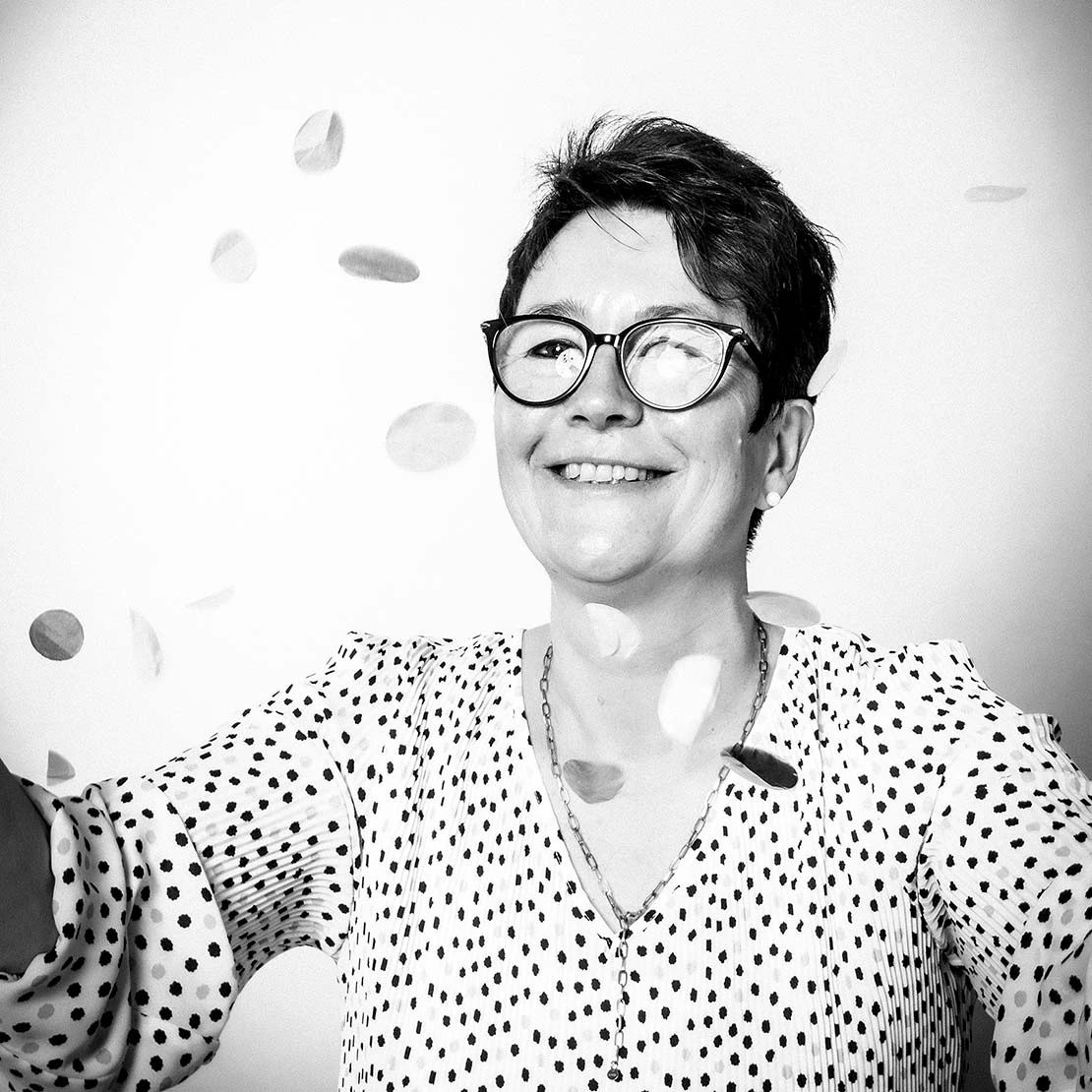 Mitarbeiterfoto in schwarz-weiß von einer Frau, die Konfetti wirft und dabei lacht.  