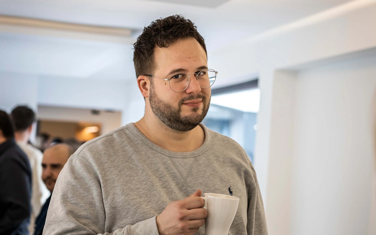 Ein Mann mit Brille während eines Workshops in der Agentur hält eine Kaffeetasse in der Hand und schaut in die Kamera.